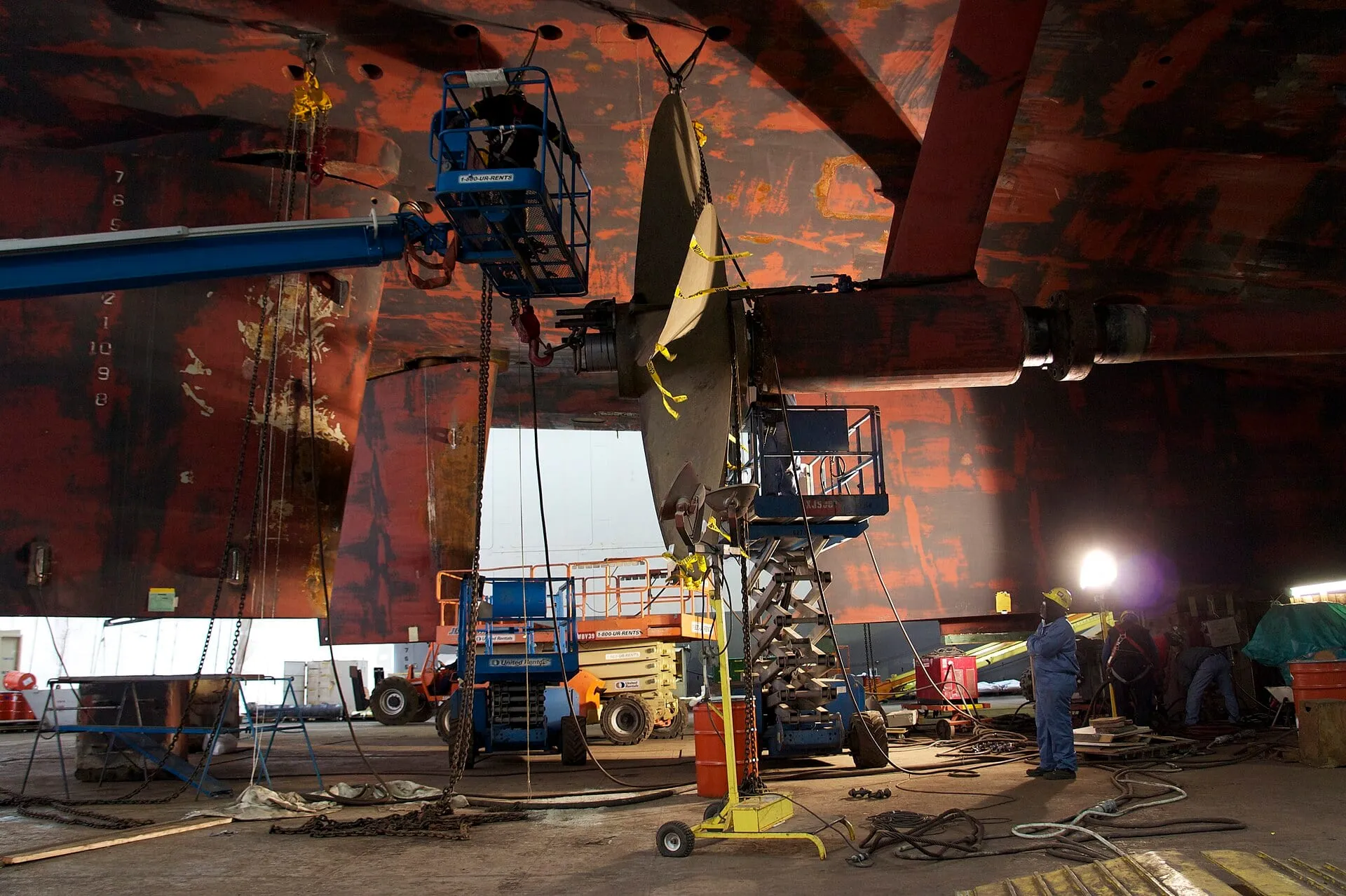 Repair crew on elevated platforms working beneath a hull in dry dock